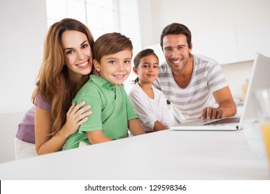 Happy Family Looking At The Camera With A Laptop In Kitchen