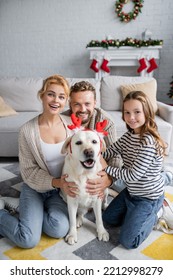 Happy family looking at camera near blurred labrador with christmas headband in living room - Shutterstock ID 2212998279