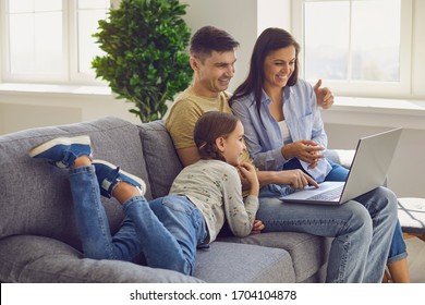 Happy family looking at a laptop while sitting comfortably on a sofa in a living room at the weekend.
