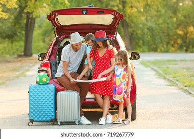 Happy Family Looking At Map Next To Car In Countryside