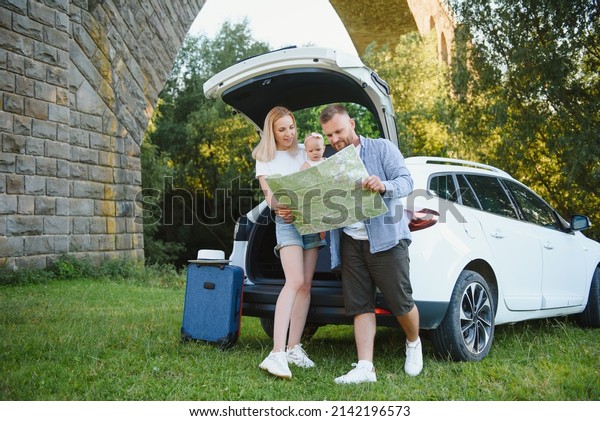 Happy family looking at\
map next to car