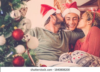 Happy Family In Love Celebrate Christmas Eve All Together With Kiss And Hug And Joy - Joyful People With Red Winter Decorations At Home - Concept Of Father And Mother And Son Together