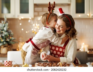 Happy Family Loving Mother And Boy Son Hugging Embracing While Cooking Together In Kitchen On Christmas, Mom And Child Baking Xmas Gingerbread Cookies During Winter Holidays