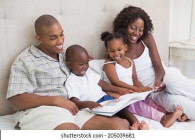 Happy Family Lying On Bed Reading Book At Home In The Bedroom