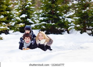 Happy Family Lying On The Snow In Winter Forest, Looking At The Camera, Horizontal Photo