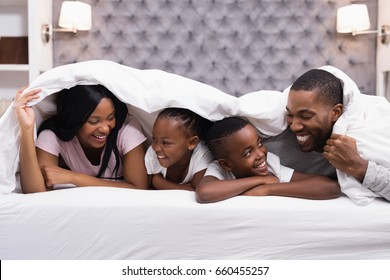 Happy family lying together under blanket on bed at home - Powered by Shutterstock