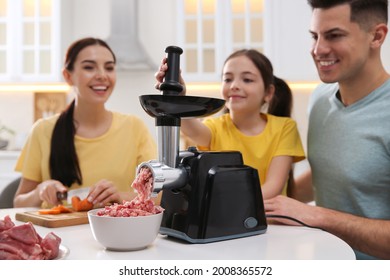 Happy Family Making Dinner Together In Kitchen, Father And Daughter Using Modern Meat Grinder While Mother Cutting Carrot