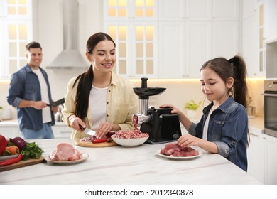 Happy Family Making Dinner Together In Kitchen, Little Girl Using Modern Meat Grinder While Her Mother Cutting Onion