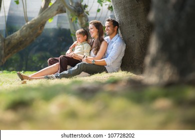 Happy Family With Man, Woman And Child Leaning On Tree In City Park. Copy Space