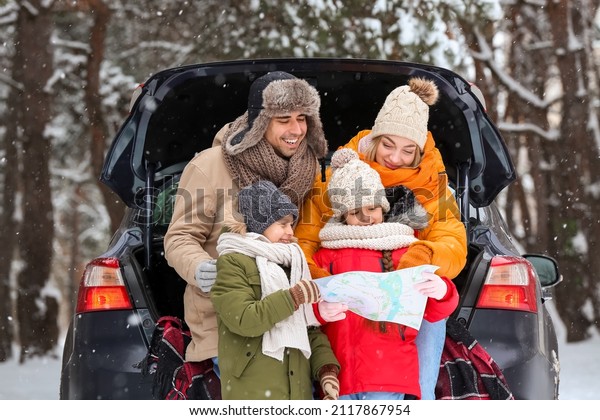 Happy family with map and car in forest on snowy\
winter day