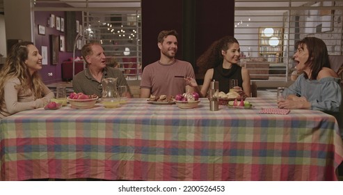 Happy Family Members Talking In The Evening While Sitting At The Table Outside In The Backyard Home Party. Joyful Group Of Friends Laughing And Smiling