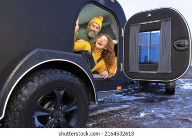 Happy Family, Middle Aged Woman And Man Peeking Out Of The Camper Door. Family Vacation Time Together At The Journey Enjoying Time In Camper Trailer. Camper Trailer Vacation, Journey Concept. 