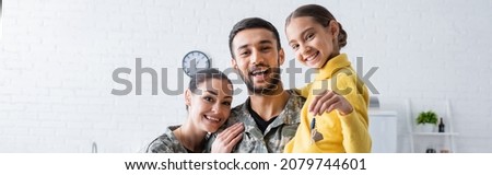 Happy family in military uniform holding daughter with key at home, banner