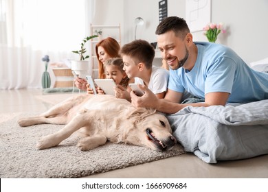 Happy Family With Modern Devices And Dog In Bedroom At Home