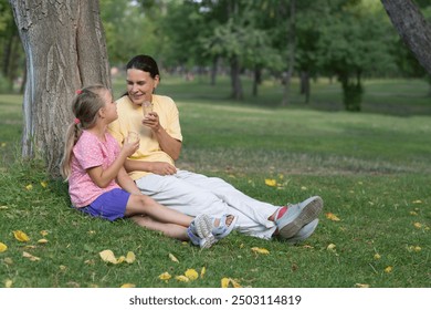 Happy family mom and child daughter eats ice cream having fun and doing picnic outdoor at city park on the green grass in summer day. Happy childhood. copy space - Powered by Shutterstock