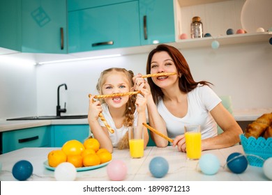 Happy Family, Mom And Daughter Are Sitting In The Kitchen And Eating Bread Sticks. Family Relations Of The Child With The Parents