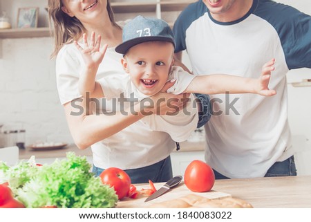 Happy family of mom, son and father are cutting vegetables on salad  and having fun together in kitchen. 