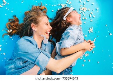 Happy Family Moments Of Joyful Mother Tickling Her Little Daughter On Blue Floor. Having Fun In Popcorn, Crazy Funny Weekends With Lovely Kids, Expressing Happiness