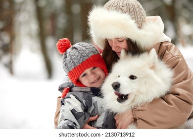 Happy Family Moments, Winter Games Concept. Side View Of Happy Mother Carrying And Hugging Cute Little Son Together While Standing Against Snowy Trees In Forest Or Park.