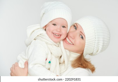 Happy Family: Mother And Baby Daughter In White Winter Hats Laughing On A Gray Background