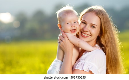 Happy Family Mother And Baby Hugging In A Meadow  Yellow Flowers On Nature In Summer
