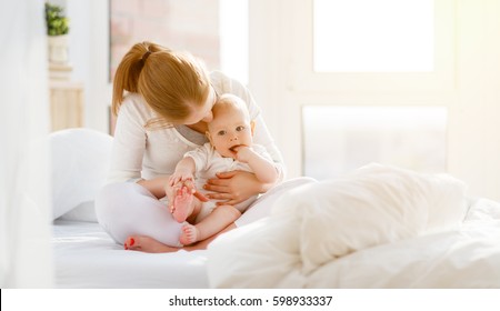 Happy Family Mother And Baby Playing, Hugging And Laughing In Bed
