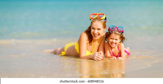 Happy family mother and chid daughter in masks for swimming on the beach in summer