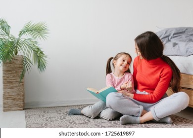 Happy Family Mother And Child Daughter Reading Holding Book Lying In Bed, Smiling Mom Baby Sitter Telling Funny Fairy Tale To Cute Preschool Kid Girl Having Fun Laughing Together With Bedtime Stories