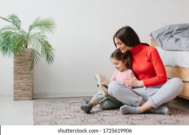 Happy Family Mother And Child Daughter Reading Holding Book Lying In Bed, Smiling Mom Baby Sitter Telling Funny Fairy Tale To Cute Preschool Kid Girl Having Fun Laughing Together With Bedtime Stories