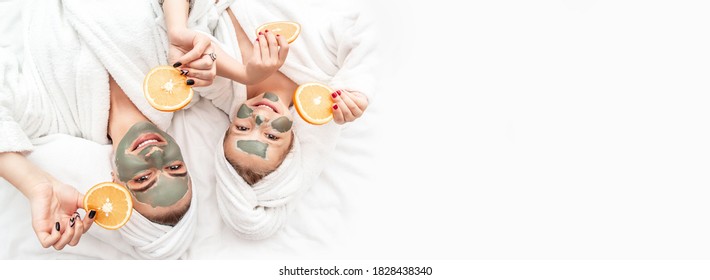 Happy family mother and child daughter make face skin mask with towel on head, holding slices of oranges on white background, Facial skin care, cosmetology Long banner format. - Powered by Shutterstock