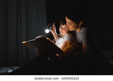 happy family mother and child son reading a book with a flashlight. Family before going to bed mother reads to her child son book near a flashlight in the evening.