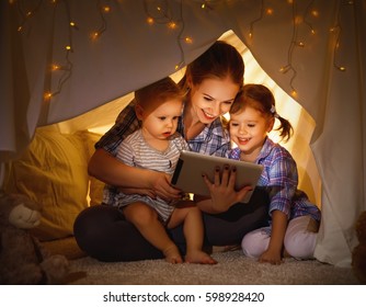 Happy family mother and children playing in tablet  pc in a tent evening in dark
