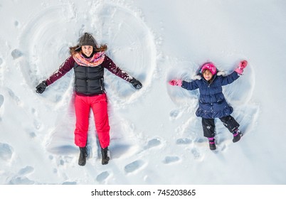 Happy Family, Mother And Cute Daughter Making Snow Angel While Lying On Snow. 