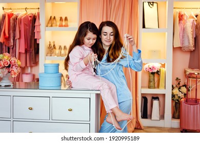 Happy family. Mother and daughter in blue and pink silk pajamas in the dressing room are having fun choosing pearl beads.