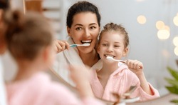 Happy Family! Mother And Daughter Child Girl Are Brushing Teeth Toothbrushes In The Bathroom.