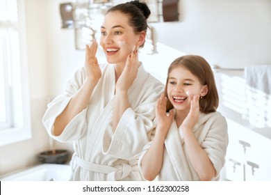 Happy Family! Mother And Daughter Child Girl Are Caring For Skin In The Bathroom.