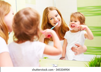 Happy Family Mother And Daughter Child Girl Brushing Her Teeth Toothbrushes Front Of The Mirror In The Bathroom