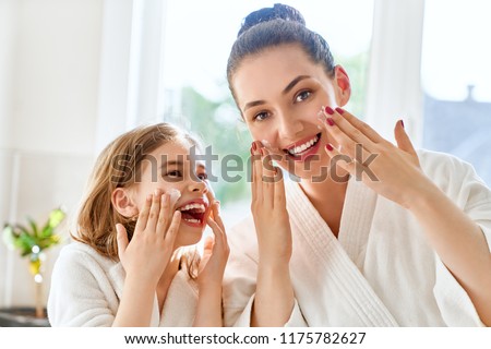 Happy family! Mother and daughter child girl are caring for skin in the bathroom.