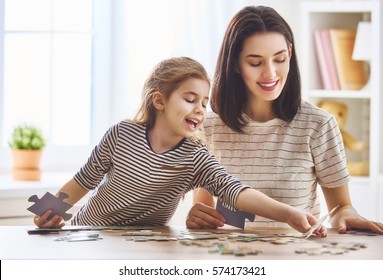 Happy Family. Mother And Daughter Do Puzzles Together. Adult Woman Teaches Child To Solve Puzzles.