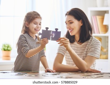 Happy family. Mother and daughter do puzzles together. Adult woman teaches child to solve puzzles.