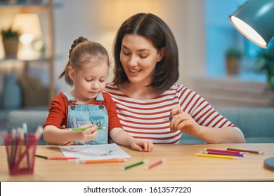 Happy family. Mother and daughter drawing together. Adult woman helping to child girl.