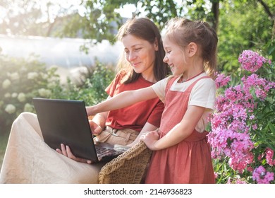 Happy Family Mother And Daughter Look At Laptop Computer Monitor In Backyard In Garden In Summer. Remote Work. Online Shopping.