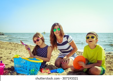 Happy Family Mother, Daughter And Son Having Fun On Beach Sand. Parent Mom And Children Kids With Toys At Sea. Summer Vacation Holidays Relax And Happiness.