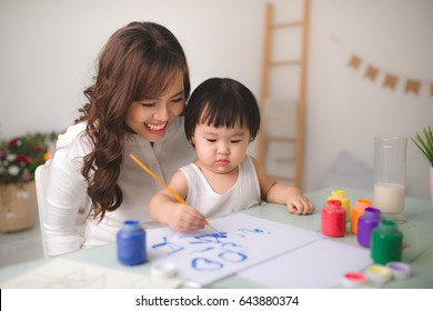 Happy family mother and daughter together paint. Asian woman helps her child girl.