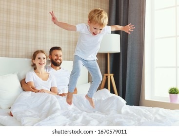 happy family mother, father and child  laughing, playing and jumping in bed     in bedroom at home