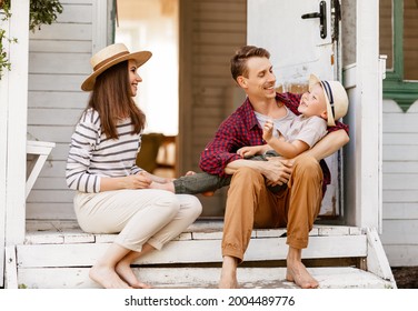 Happy Family: Mother Father And Child Son Are Sitting On The Porch, Laughing And Playing In The Summer At The Dacha Country House