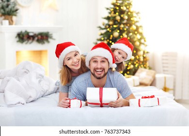 Happy Family Mother Father And Child On Christmas Morning In Bed In Pajamas Open Gifts
