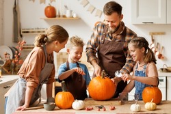 Happy Family Mother, Father  And Children Daughter And Son To Remove   Pulp From Pumpkin While Carving Jack O Lantern With Family In Cozy Kitchen At Home, Parents With Kids Preparing For Halloween