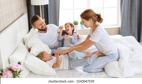 happy family mother, father and children laughing, playing and tickles in bed in bedroom at home