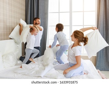 happy family mother, father and children laughing, playing, fights pillows and jumping in bed in bedroom at home